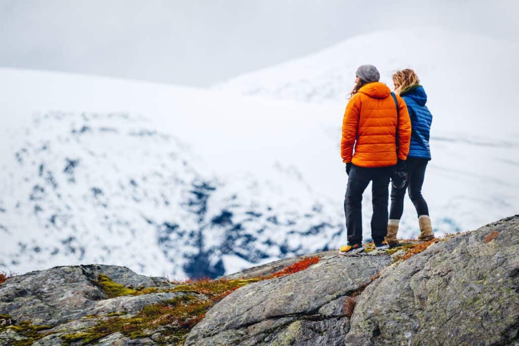 Couple in down jackets looking at snow covered hillside.