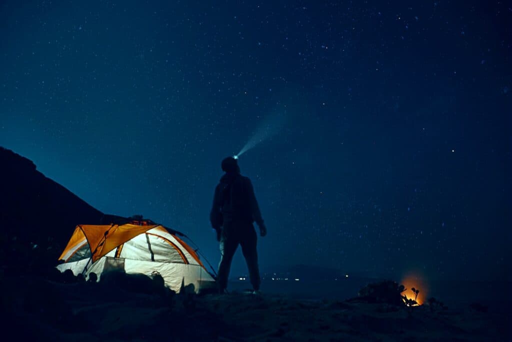 Man standing outside his tent, staring up at the stars at night.