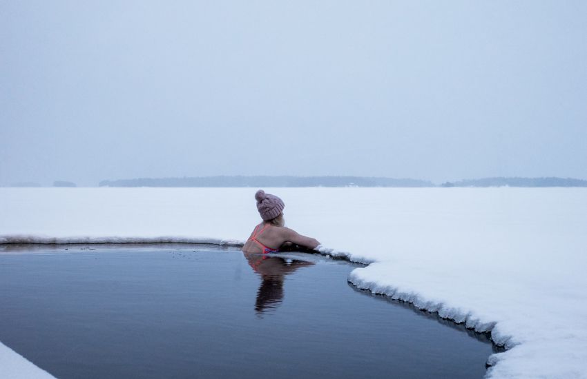 Woman relaxing in cold icy water surrounded by snow.