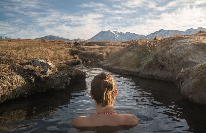 The Benefits of Cold Water Swimming - Woman relaxing in cold water stream with a view of the mountains