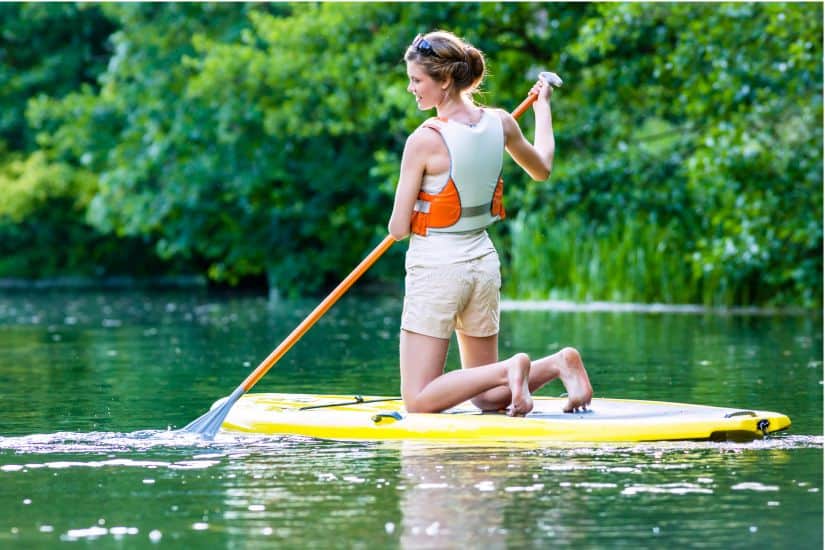 Paddle board safety - Girl kneeling on paddle board wearing a life jacket.