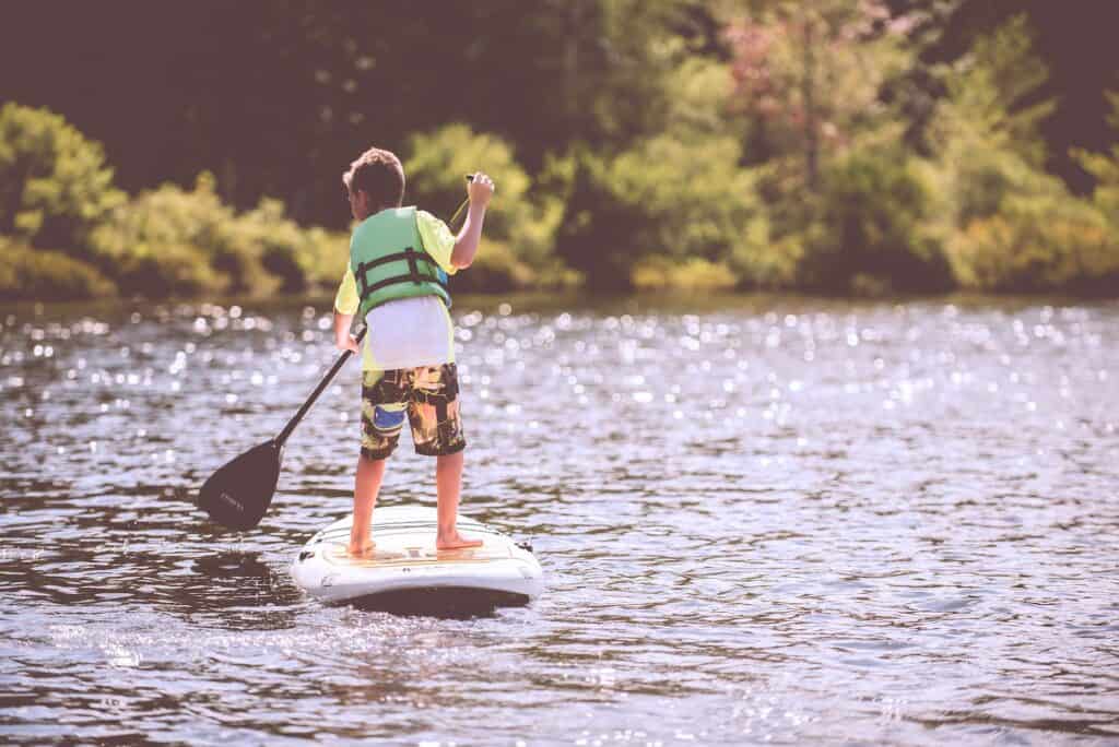 Child wearing a life jacket whilst paddling on a stand up paddle board.