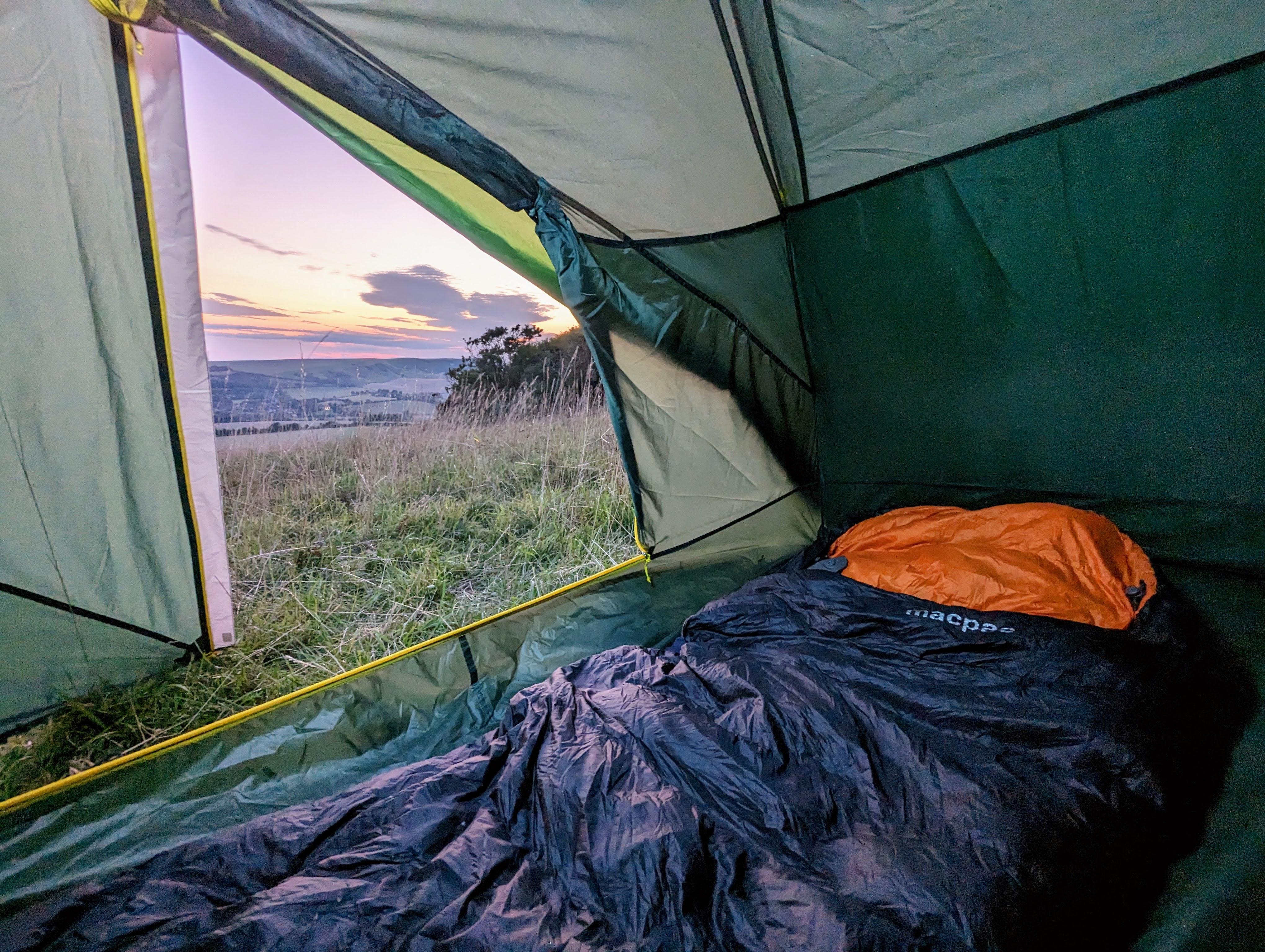 Sleeping bag laid out inside a tent with a view of the sunset