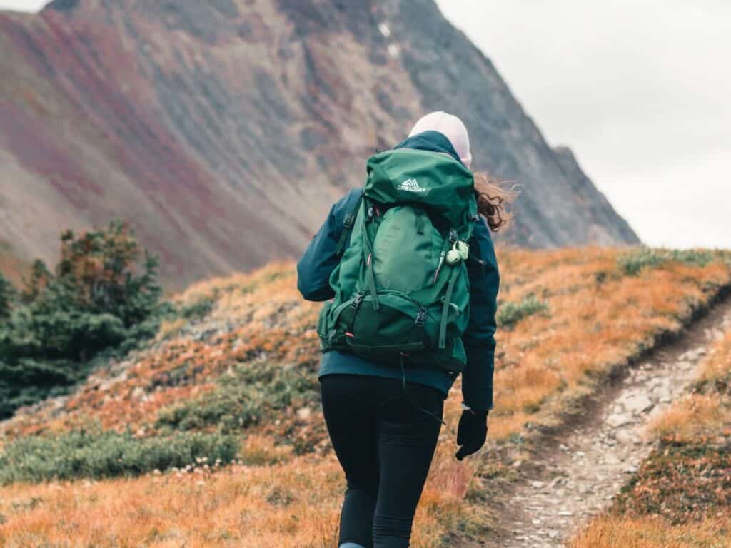 Woman Hiking up a mountain wearing a green backpack